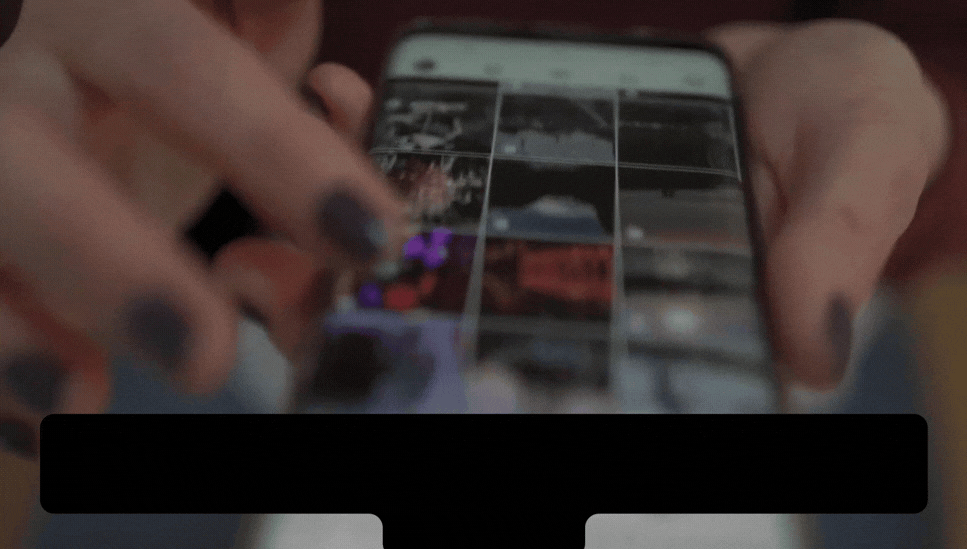 Close-up of hands holding a smartphone with a photo gallery grid on screen, the user taps a photo with a finger