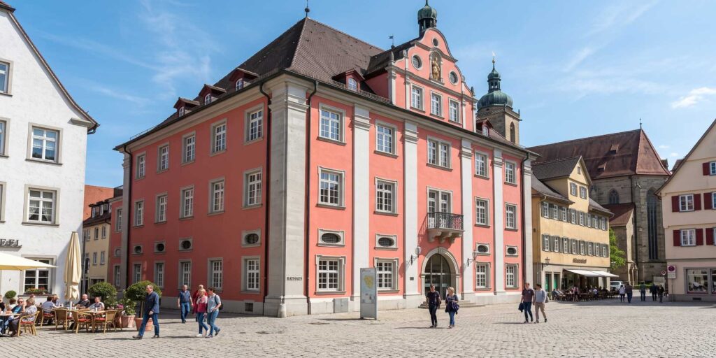 Pink town hall building in a European square with outdoor café, pedestrians and a blue sky.